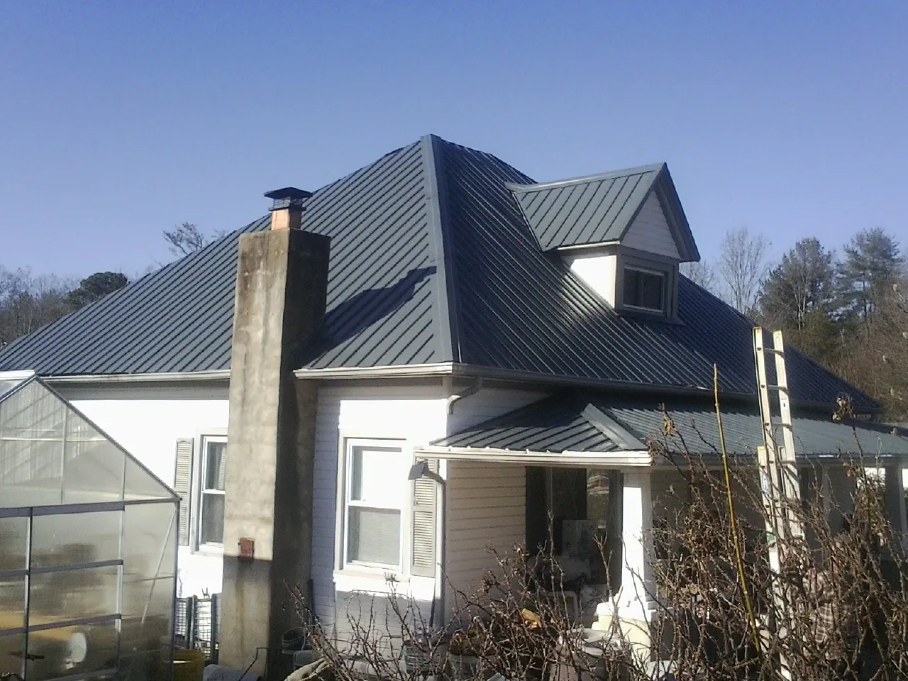 Dark blue standing seam metal roof on a white farmhouse with dormer — Slate & Tile Roof Repair by Roofing Brothers in Galvin