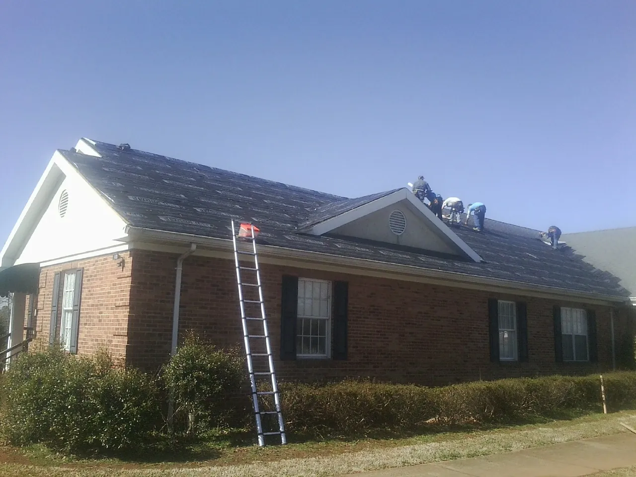 Crew tearing shingles off a brick ranch roof with a ladder set — Emergency Roof Repair work by our crew in Galvin