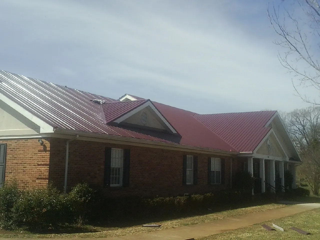 Red metal roof with gabled entries on a long brick building, from a Hail Damage Roof Repair job in Galvin