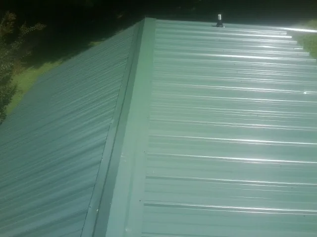 New green metal panels meeting at the ridge of a roof — Flat Roof Repair work by our crew in Galvin