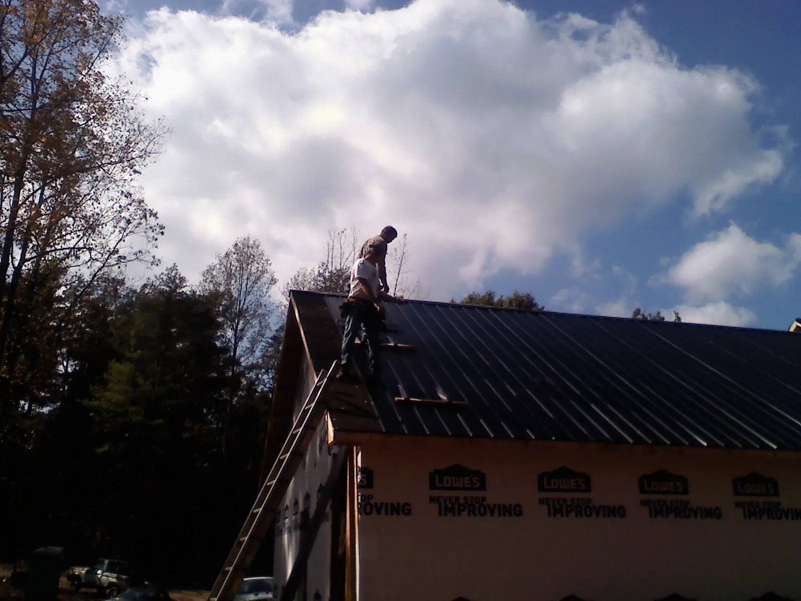 Roofer fastening dark metal panels high against a cloudy sky, from a Roof Inspection job in Galvin
