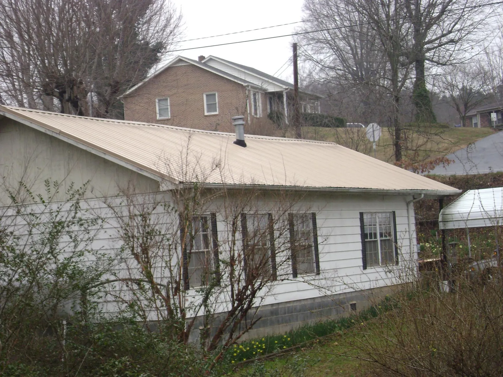 Tan metal roof on a white sided house set into a hillside — Commercial Roofing by Roofing Brothers in Galvin