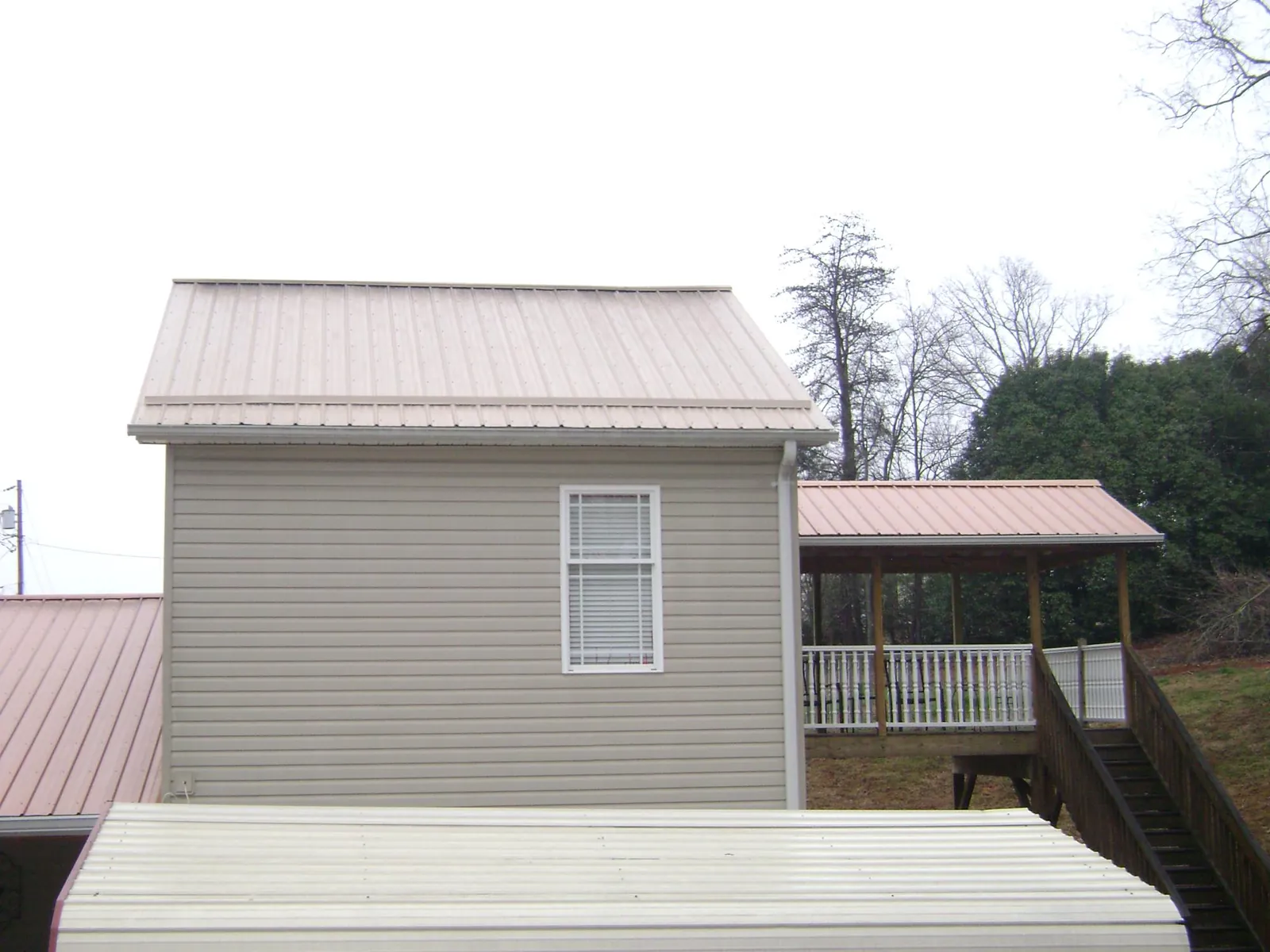 Tan metal roofs on a two story addition and attached porch, from a Roof Replacement job in Galvin
